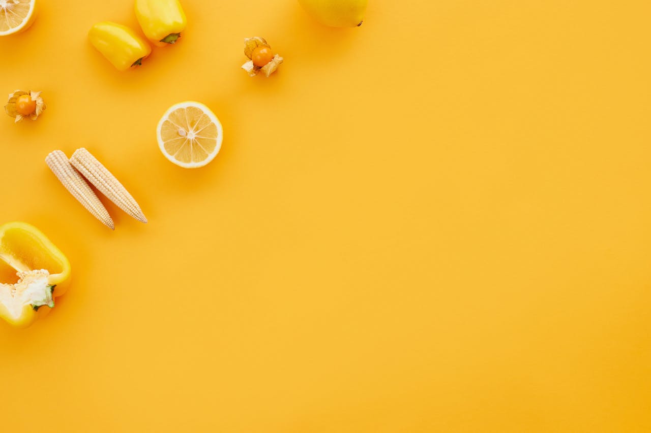 A colorful flat lay of yellow fruits and vegetables on a vibrant yellow background.